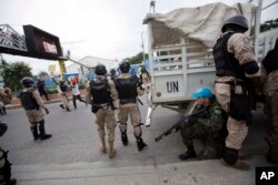 FILE - A U.N. peacekeeper takes cover behind national police officers while demonstrators throw rocks, during a protest against the country's electoral council to mark the 25th anniversary of first democratic election in 1990, in Port-au-Prince, Haiti.