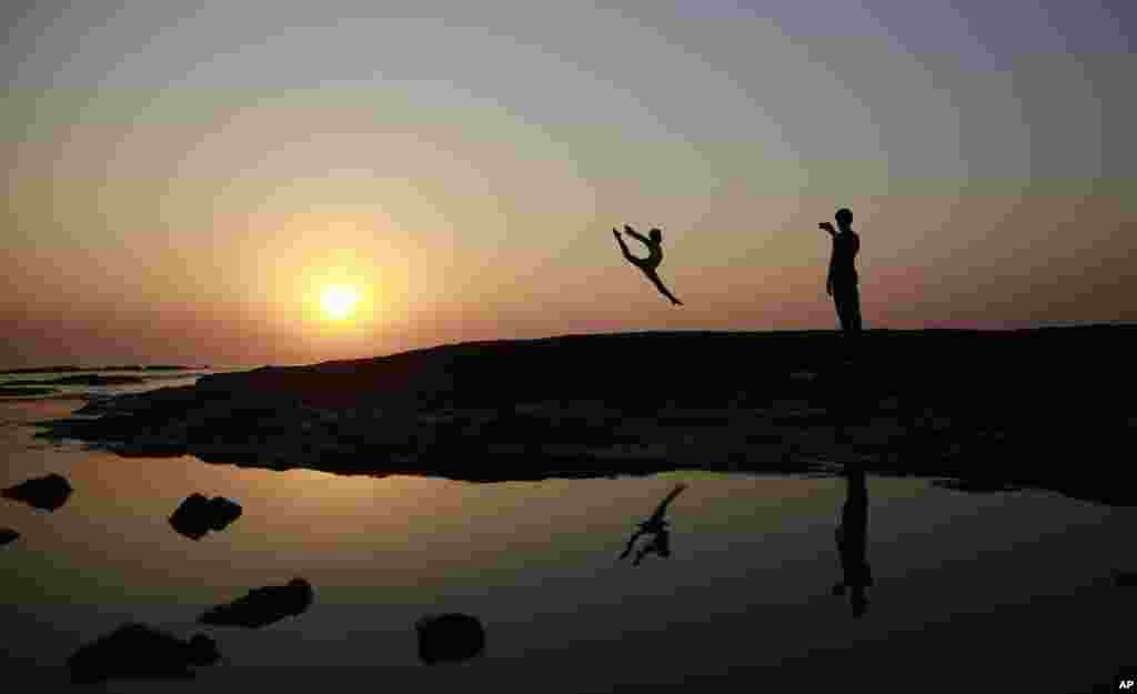 An Indian dancer taking pictures of his partner is silhouetted against the sky and reflected in the water during the last sunset of the year, on the Arabian Sea coast in Mumbai.