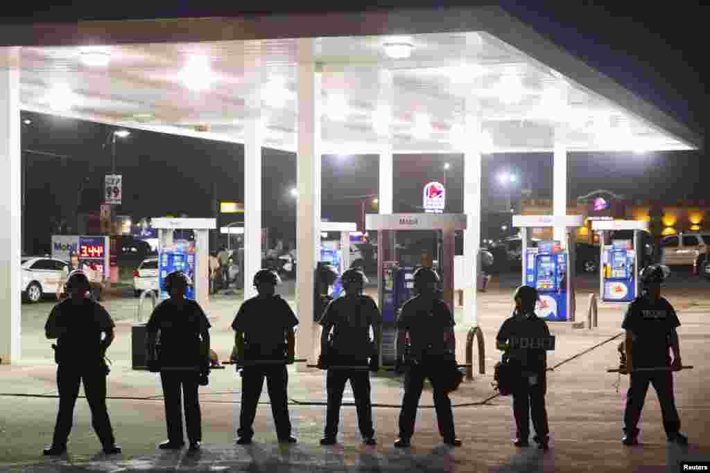 Police officers stand guard at a gas station after protests against the shooting of Michael Brown turned violent near Ferguson, Missouri, Aug. 17, 2014.