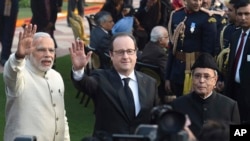 French President Francois Hollande, flanked by Indian Prime Minister Narendra Modi, left and Indian President Pranab Mukherjee, waves to the media at a reception hosted by the Indian President to mark India's Republic Day in New Delhi, Jan. 26, 2016.