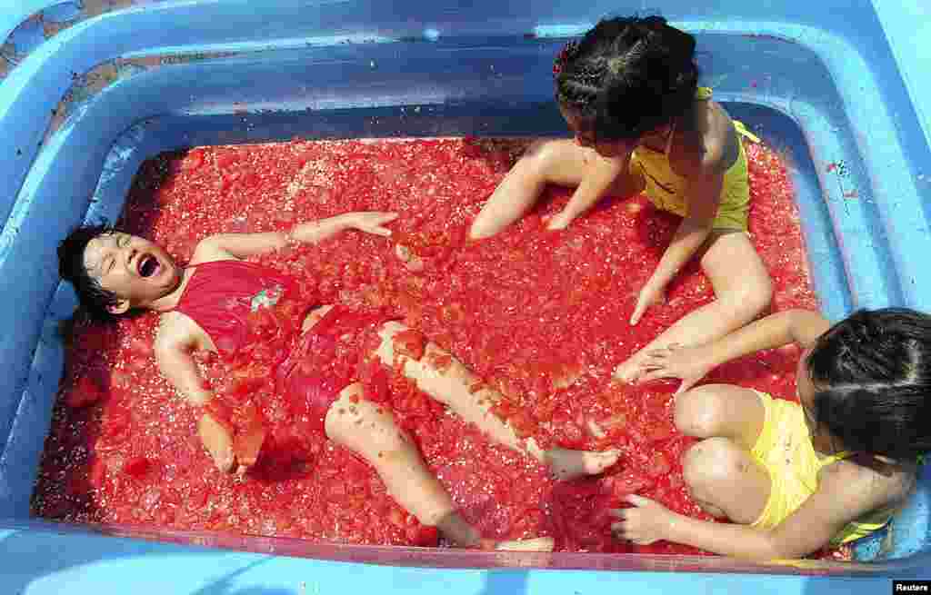 Children play in a inflatable pool filled with smashed watermelons to cool off, at an amusement park in Hangzhou, Zhejiang province, China.