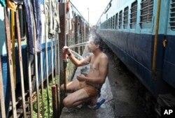 FILE - An Indian passenger takes a bath beside rail tracks on a hot summer day at a railway station in Jammu, India, May 25, 2015.