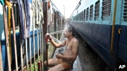 An Indian passenger takes a bath beside rail tracks on a hot summer day at a railway station in Jammu, India, Monday, May 25, 2015. Severe heat wave conditions continue to prevail at several places in northern India with temperatures reaching 48 degrees C