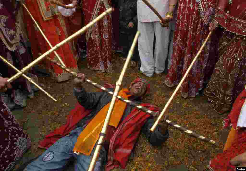 Seorang pria melindungi dirinya dari seorang perempuan yang bercanda dan memukulinya dengan tongkat sebagai bagian dari perayaan Holi di desa Gokul di distrik Mathura di negara bagian India utara, Uttar Pradesh.