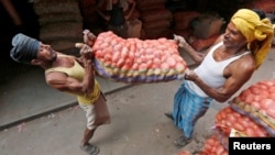 FILE- Laborers lift a sack of potatoes to load onto a supply truck at a wholesale market in Kolkata, India, Oct. 14, 2016.