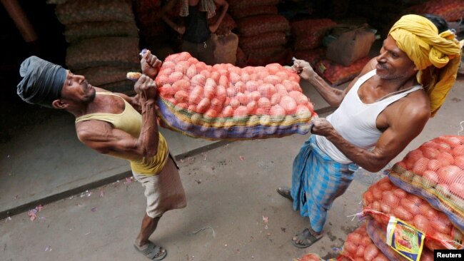 FILE- Laborers lift a sack of potatoes to load onto a supply truck at a wholesale market in Kolkata, India, Oct. 14, 2016.
