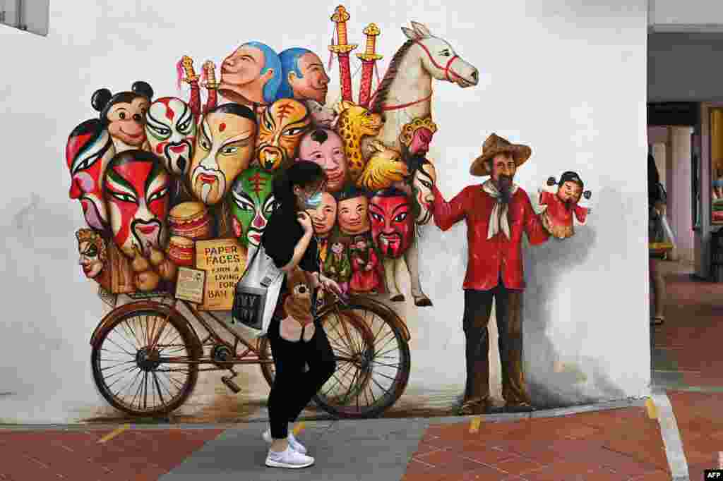 A woman walks past a mural on a wall along a street in Singapore.