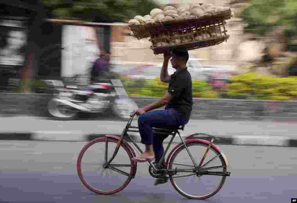 Seorang penjual roti menyunggi dagangannya di atas kepala sambil bersepeda di Kairo, Mesir.