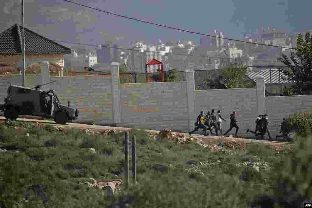 Palestinian protesters run away as an Israeli security vehicle chases after them during clashes following a demonstration against the expansion of settlements in the town of Salfit, in the Israeli-occupied West Bank.