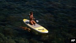 Seorang perempuan mengayuh di atas papan selancar di Laut Mediteranea di Barcelona, Spanyol. Badan cuaca di Spanyol memperingatkan masyarakat untuk lebih berhati-hati sementara gelombang panas melanda Eropa Barat (29/6).