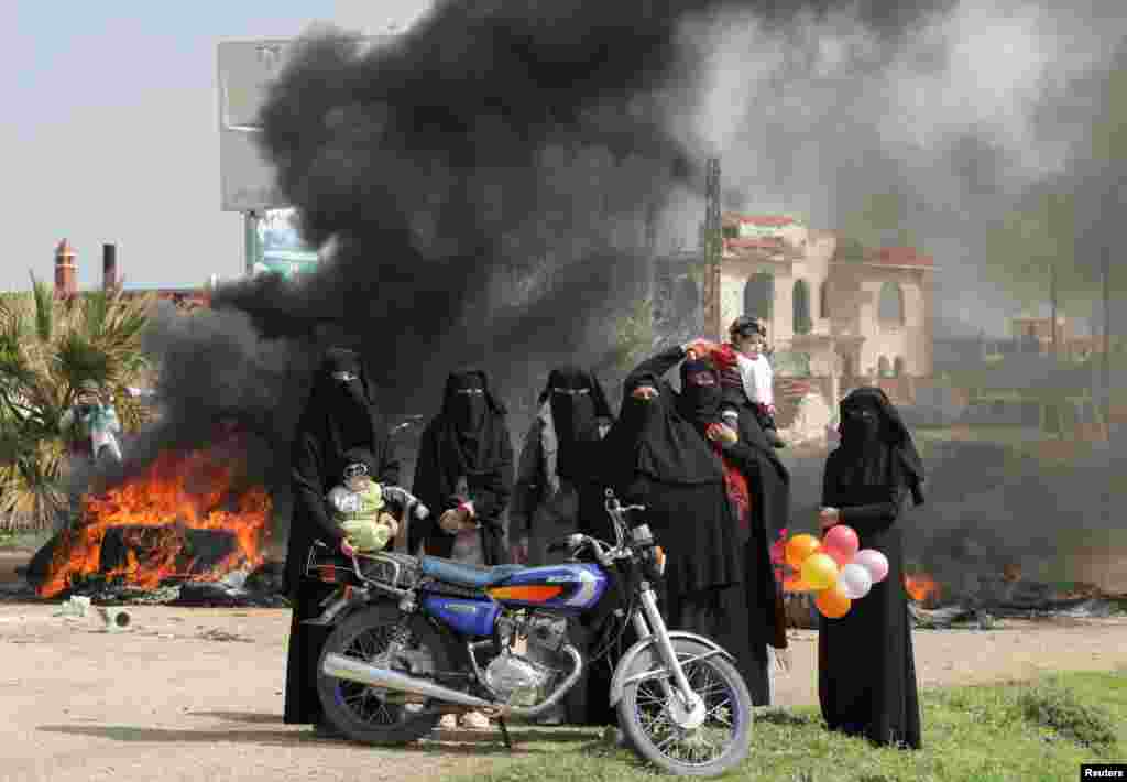 Women stand near burning tires during a protest against the agreement on joint Russian and Turkish patrols, at M4 highway in Idlib province, Syria.