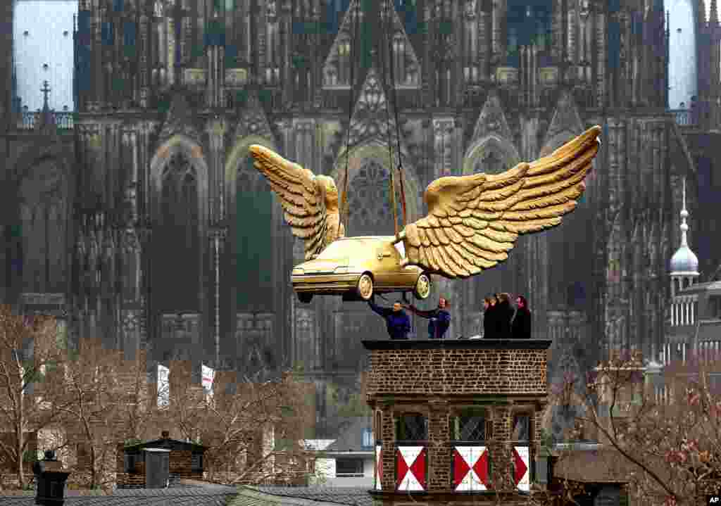 Workers help guide artist HA Schult&#39;s sculpture &quot;Fluegelauto,&quot; a golden winged Ford Fiesta, onto the roof of the City Museum in Cologne, Germany. In the background is the Cologne Cathedral.