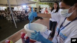FILE - A woman demonstrates how to clean a toilet bowl at a poor community in Manila, Philippines, on World Toilet Day, an event aimed at improving access to basic sanitation, Nov. 19, 2014.