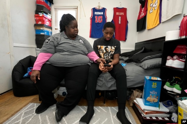 LaTonya Peterson sits with her son Joshua Jackson, 16, as he attends school on his phone at home in Detroit, Friday, Jan. 7, 2022. (AP Photo/Paul Sancya)