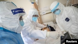 2020年2月16日，身穿防護服的武漢紅十字會醫院的醫護人員在照看一位被隔離的新冠病毒感染病人。