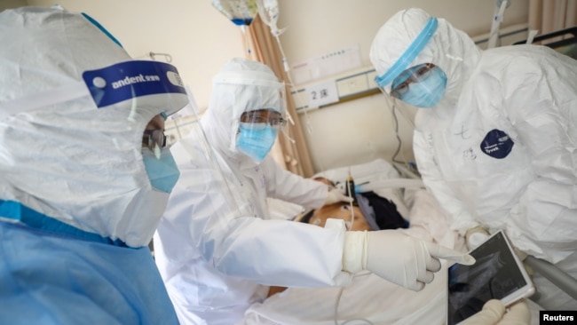 2020年2月16日，身穿防护服的武汉红十字会医院的医护人员在照看一位被隔离的新冠病毒感染病人。