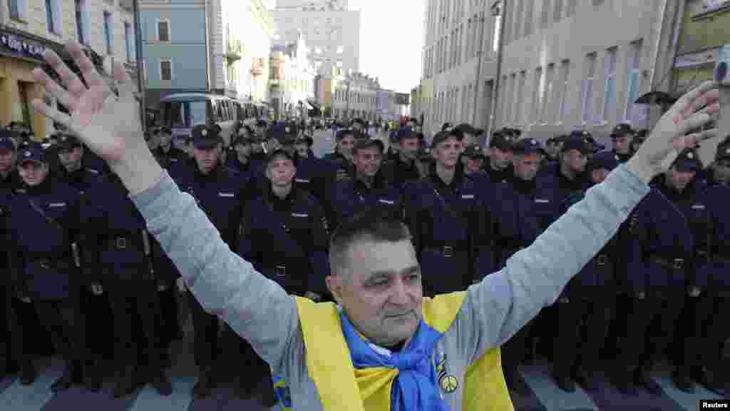 A man with a Ukrainian flag on his shoulders stands near a riot police line standing guard during an anti-war rally in Moscow, Sept. 21, 2014. 