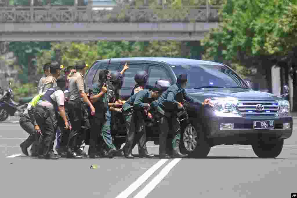 Agentes policiais protegem-se atras de carro durante troca de tiros com atacantes perto de um dos locais onde se registou a explosão em Jacarta (14 Janeiro 2016). Outras explosões tiveram lugar junto a um café da cadeia Starbucks numa movimentada área comercial da capital indonésia. &nbsp;