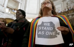 The Rev. Annie Steinberg-Behrman (right) provisional pastor with Metropolitan Community Church, holds a sign while listening to speakers at a meeting at City Hall in San Francisco to reaffirm the city's commitment to being a sanctuary city, Nov. 14, 2016.