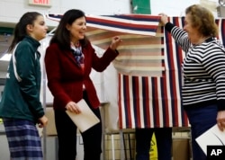 A poll worker lifts the curtain as Sen. Kelly Ayotte, R-N.H., center, leaves the voting booth with her daughter, Kate, Nov. 8, 2016, at Charlotte Avenue Elementary School in Nashua, N.H.