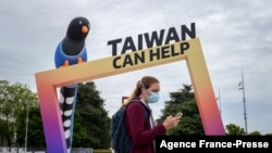 A woman walks by an arch reading "Taiwan can help" next to the building of the United Nations Offices in Geneva on the opening day of the WHO's World Health Assembly on May 24, 2021 in Geneva.