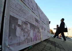 Pejalan kaki melewati foto penjaga yang menurunkan anak-anak "Brothers Home" dari truk di Busan, Korsel, yang dipajang di depan Majelis Nasional di Seoul, Korea Selatan, 2 April 2019. (Foto: dok)