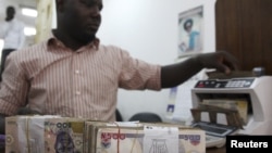 A money dealer counts the Nigerian Naira on a machine in his office in the commercial capital of Lagos, Nigeria. 