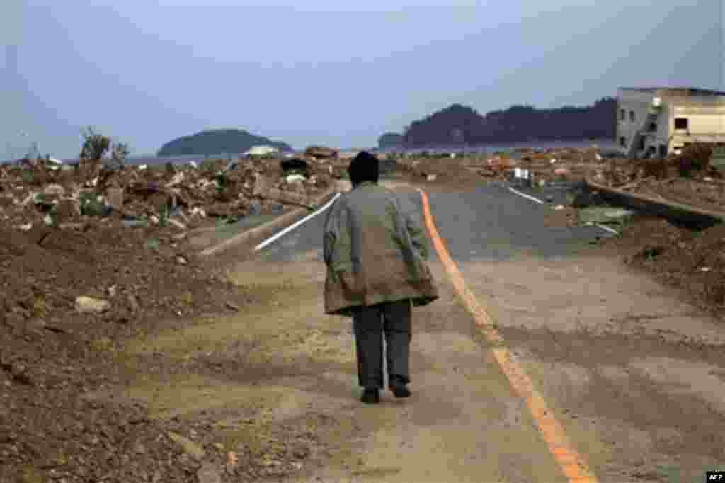 A Japanese earthquake and tsunami survivor walks alone on a road past the destroyed village of Saito, in northeastern Japan, Monday, March 14, 2011. (AP Photo/David Guttenfelder)
