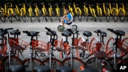 FILE - A child rides past bicycles from bike-sharing companies parked along a sidewalk in Beijing, Aug. 31, 2017. A report says China’s factory activity expanded in September at the fastest pace in five years, indicating a healthy outlook for the world’s 