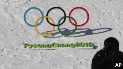 In this Friday, Feb. 3, 2017 photo, a man walks by the Olympic rings with a sign of 2018 Pyeongchang Winter Games.