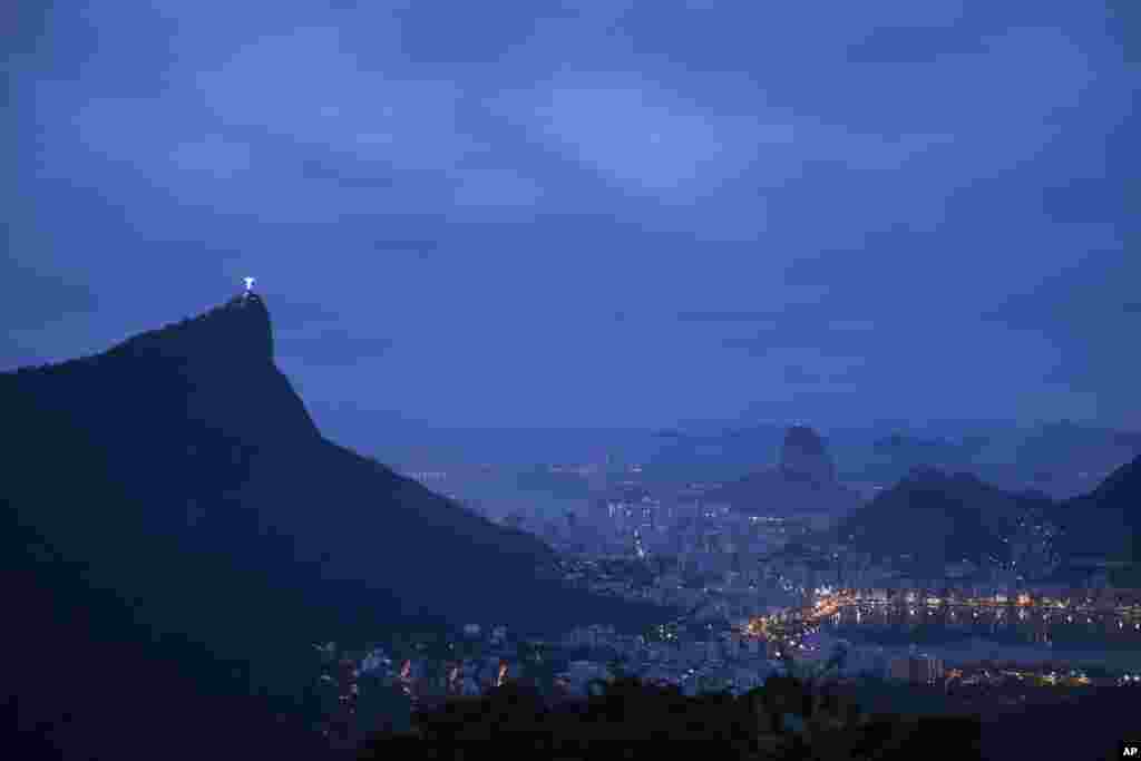 The Christ the Redeemer statue stands atop the Corcovado Mountain, left, at dawn in Rio de Janeiro, Brazil.&nbsp; The Lagoa Rodrigo de Freitas, seen illuminated at right, will host the rowing and canoe sprint events.&nbsp;