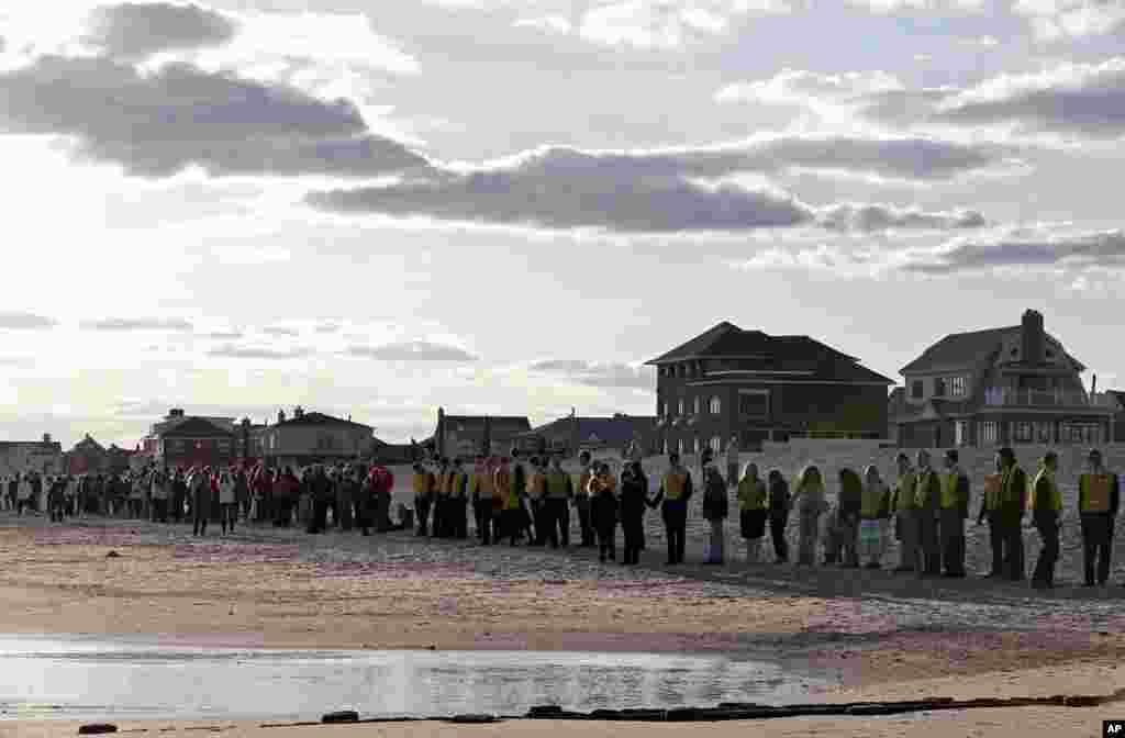 People line up along the beach in the Belle Harbor section of the Rockways during the "Rockaway Rising: Hands Across the Sand," beachside ceremony commemorating the one year anniversary of Superstorm Sandy, Oct. 27, 2013, in New York. 