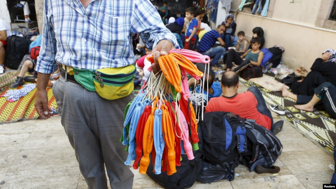 FILE - A street vendor sells balloons which can be used to waterproof mobile phones in the backyard of a mosque filled with Syrian refugees waiting to sail to Greek islands, in Izmir, Turkey, Aug. 10, 2015.