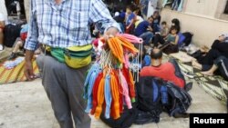 FILE - A street vendor sells balloons which can be used to waterproof mobile phones in the backyard of a mosque filled with Syrian refugees waiting to sail to Greek islands, in Izmir, Turkey, Aug. 10, 2015.