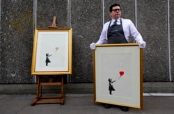 FILE - Two versions of the iconic "Girl with Balloon," by anonymous street artist Banksy, are displayed during a photo-call near one of the original locations the artwork appeared at, on the Southbank in London, Aug. 30, 2019.