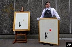 FILE - Two versions of the iconic "Girl with Balloon," by anonymous street artist Banksy, are displayed during a photo-call near one of the original locations the artwork appeared at, on the Southbank in London, Aug. 30, 2019.