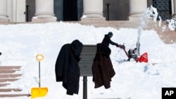 Workers jackets hang on a sign as they clear snow from the steps of the West Building of the National Gallery of Art in Washington, Jan. 25, 2016. 