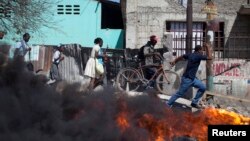 Wargamelewati barikade yang dibakar dalam protes-protes di Croix des Bouquets di pinggiran kota Port-au-Prince, Hairi (2/2). (Reuters/Andres Martinez Casares)