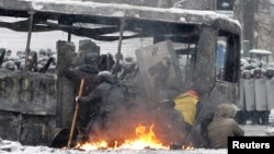 Pro-European protesters take cover behind a burnt bus during clashes with riot police in Kyiv, Jan. 22, 2014.