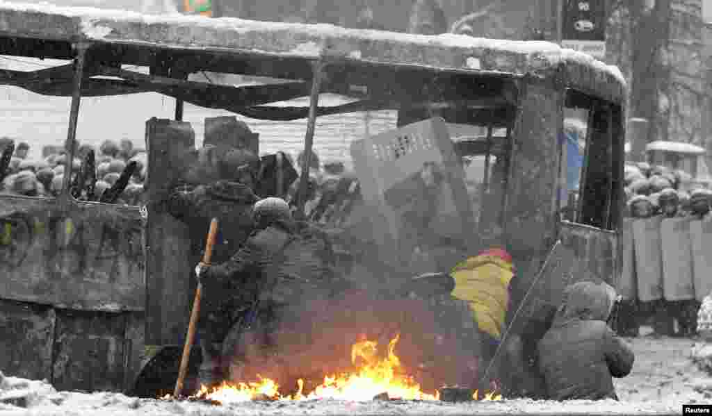 Pro-European protesters take cover behind a bus during clashes with riot police in Kyiv, Jan. 22, 2014.