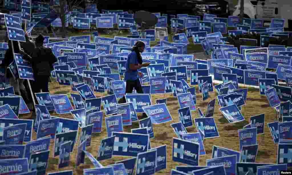 Seorang pendukung Hillary Clinton berjalan melewati poster kampanye Clinton dan saingannya dari Partai Demokrat Bernie Sanders di luar Gaillard Center sebelum debat kandidat presiden AS dari Partai Demokrat yang ditayangkan langsung di NBC News-YouTube di Charleston, South Carolina, 17 Januari 2016.