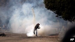 An Egyptian protester throws a tear gas canister back at riot police, not seen, during clashes near Tahrir Square, Cairo, Egypt, Sunday, Jan. 27, 2013.