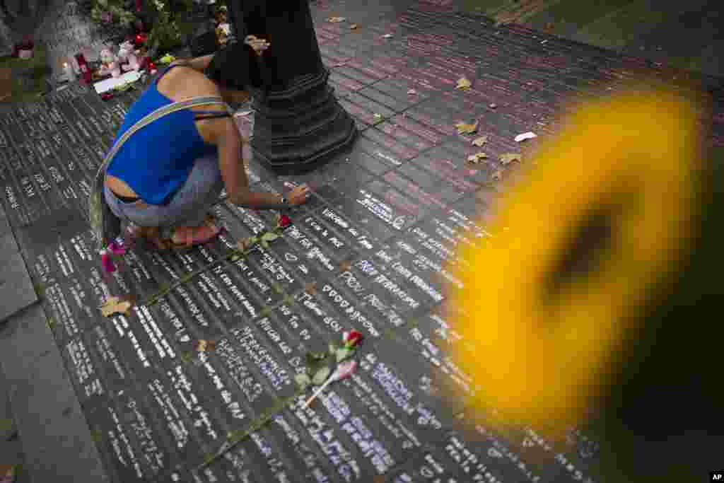 A woman writes a message on the ground as a memorial tribute after an attack that left many killed and wounded in Barcelona, Spain, Aug. 23, 2017.