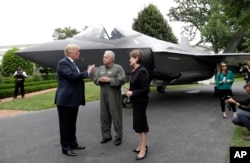 ປະທານາທິບໍດີ ດໍໂນລ ທຣຳ ໂອ້ລົມ ກັບປະທານແລະຜູ້ບໍລິຫານງານ ບໍລິສັດ Lockheed Martin ທ່ານນາງ ແມຣີລິນ ຮີວສັນ (Marilyn Hewson) ແລະ ຜູ້ອຳນວຍການ ແລະຫົວໜ້ານັກບິນທົດສອບ ທ່ານແອລັນ ນໍຣມັນ (Alan Norman) ຢູ່ຕໍ່ໜ້າເຮືອບິນລົບ F-35 ຂະນະທີ່ເຂົ້າຮ່ວມໃນ "ການວາງສະແດງ ຜະລິດຕະພັນທີ່ເຮັດຢູ່ໃນອາເມຣິກາ" ທີ່ທຳນຽບຂາວ, ວັນທີ 23 ກໍລະກົດ 2018.