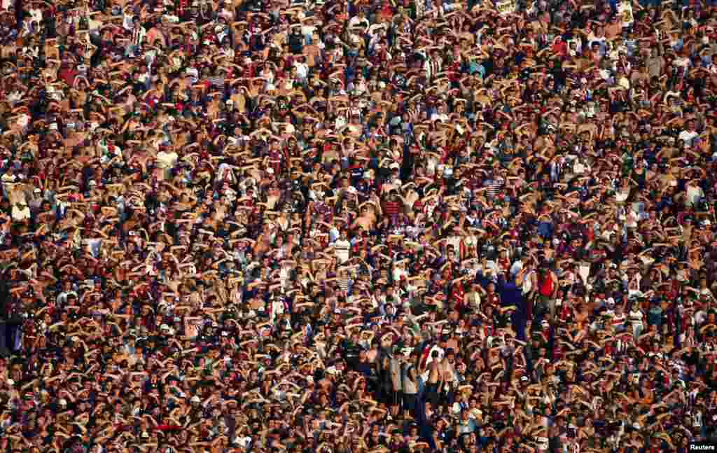 San Lorenzo&#39;s fans use their hands to block the sun during the Argentine First Division soccer match against Estudiantes in Buenos Aires, Argentina, Dec. 1, 2013. 