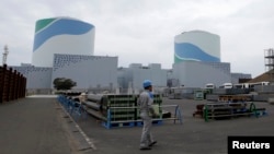 FILE - An employee of Kyushu Electric Power Co walks in front of reactor buildings at the company's Sendai nuclear power plant in Satsumasendai, Kagoshima prefecture.
