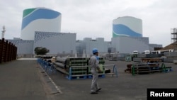 FILE - An employee of Kyushu Electric Power Co walks in front of reactor buildings at the company's Sendai nuclear power plant in Satsumasendai, Kagoshima prefecture.