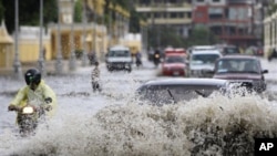 A Cambodian motorcyclist maneuvers through a flooded street along side cars on a rainy day in Phnom Penh.