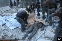 FILE - This photo released Feb. 20, 2018, by the Syrian civil defense group known as the White Helmets shows members of the group removing a victim from under the rubble of a damaged shelter that was attacked during airstrikes and shelling by Syrian government forces, in Ghouta, a suburb of Damascus, Syria.