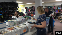 One by one volunteers pick up shampoo, toothbrush, blankets, pajamas, stuffed animals and books to put in backpack full of basic necessities. (Aline Barros/VOA)